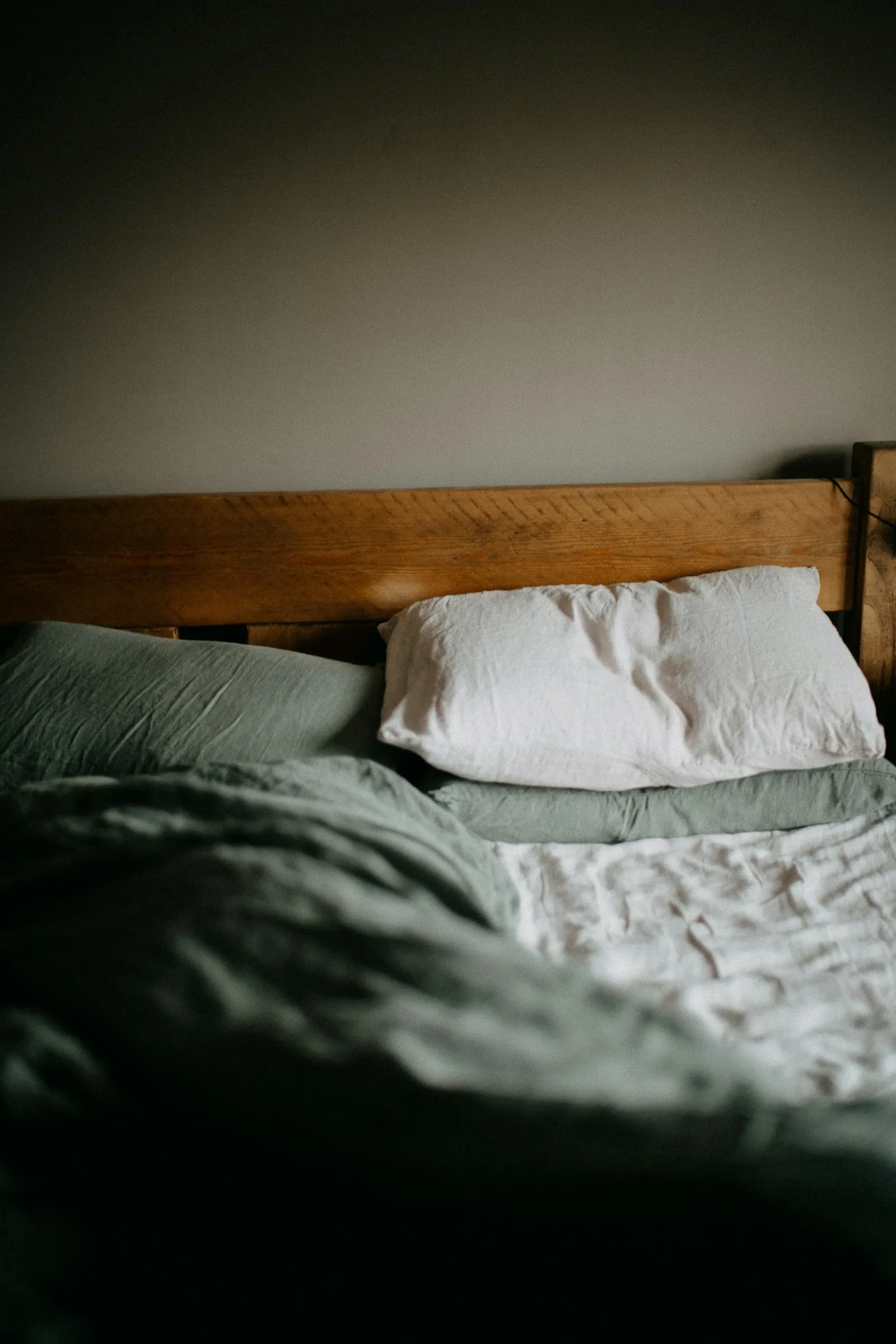 Lit en bois, deux oreillers, draps verts défaits
